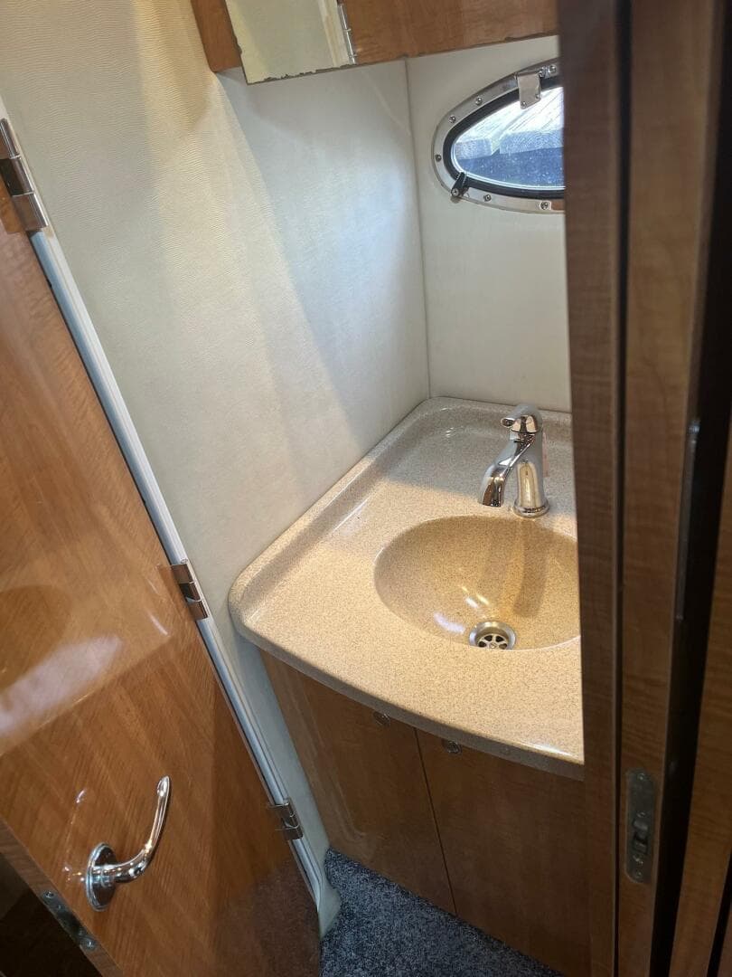 2003 Regal Commodore 3860 bathroom sink with wooden cabinetry and porthole window.