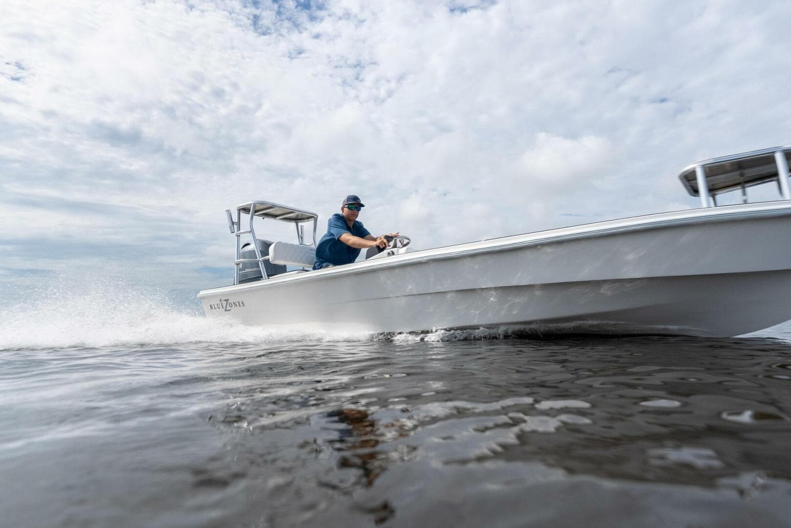 2025 BlueZones Boatworks 16' Flats boat speeding on water under cloudy sky.