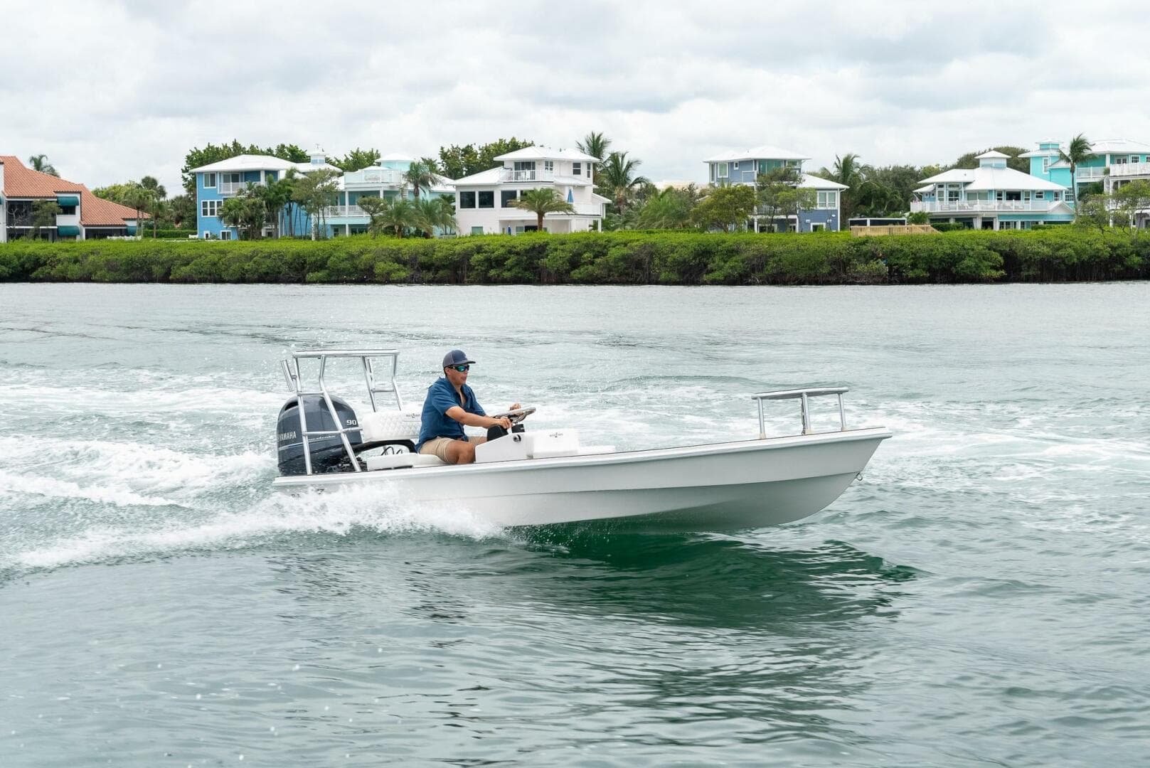 2025 BlueZones Boatworks 16' Flats cruising on water near coastal homes.