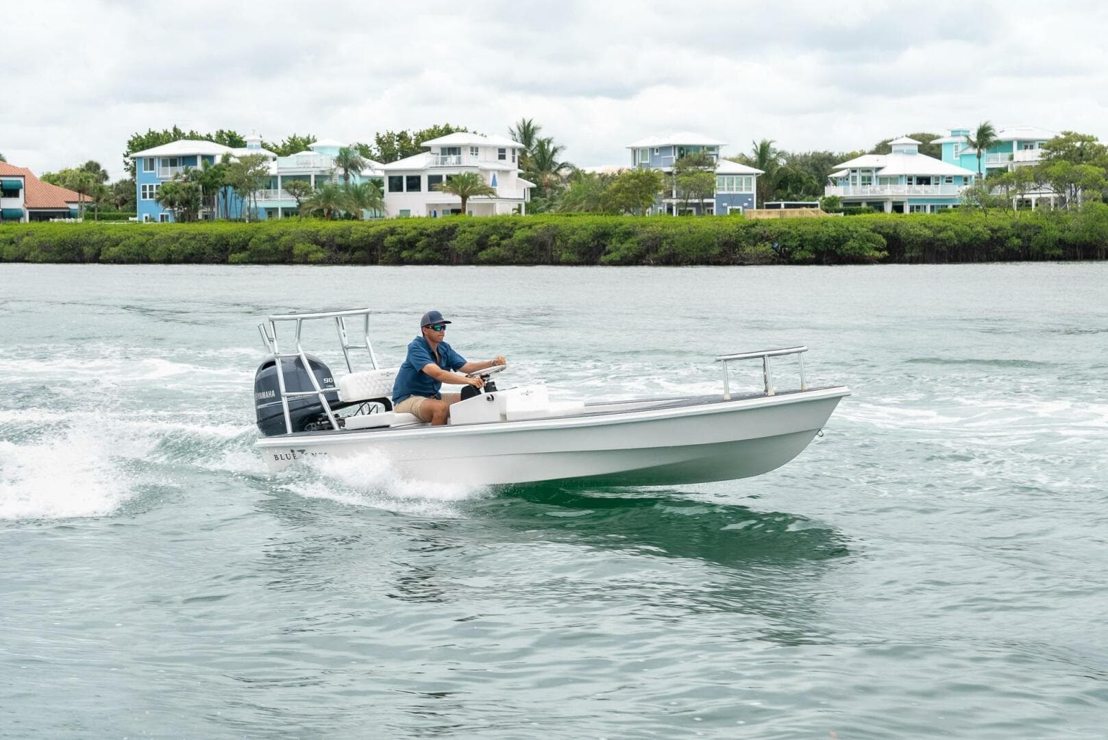 2025 BlueZones Boatworks 16' Flats cruising on water near coastal homes.