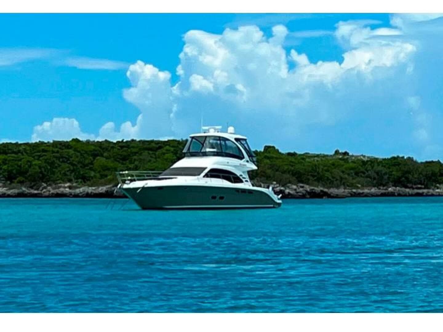 2006 Sea Ray 52 Sedan Bridge yacht on turquoise water with lush green island background.