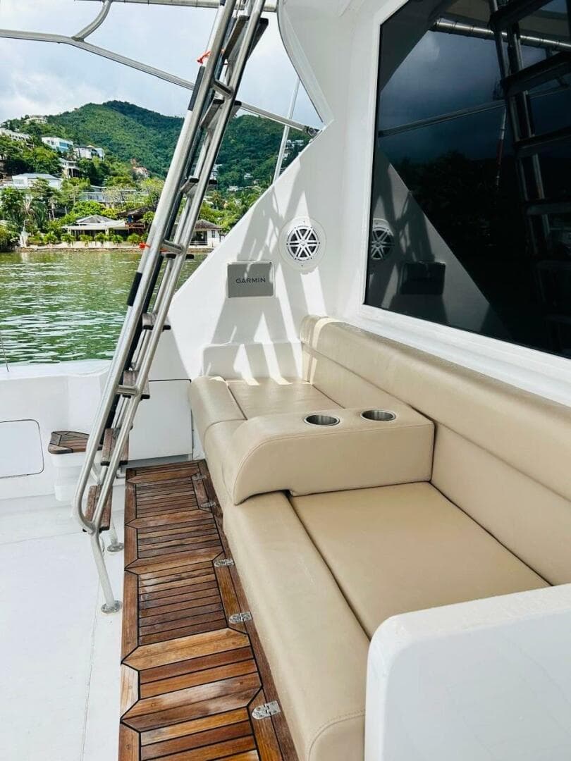 1988 Bertram 54' yacht with beige seating and wooden deck, docked by lush green hills.