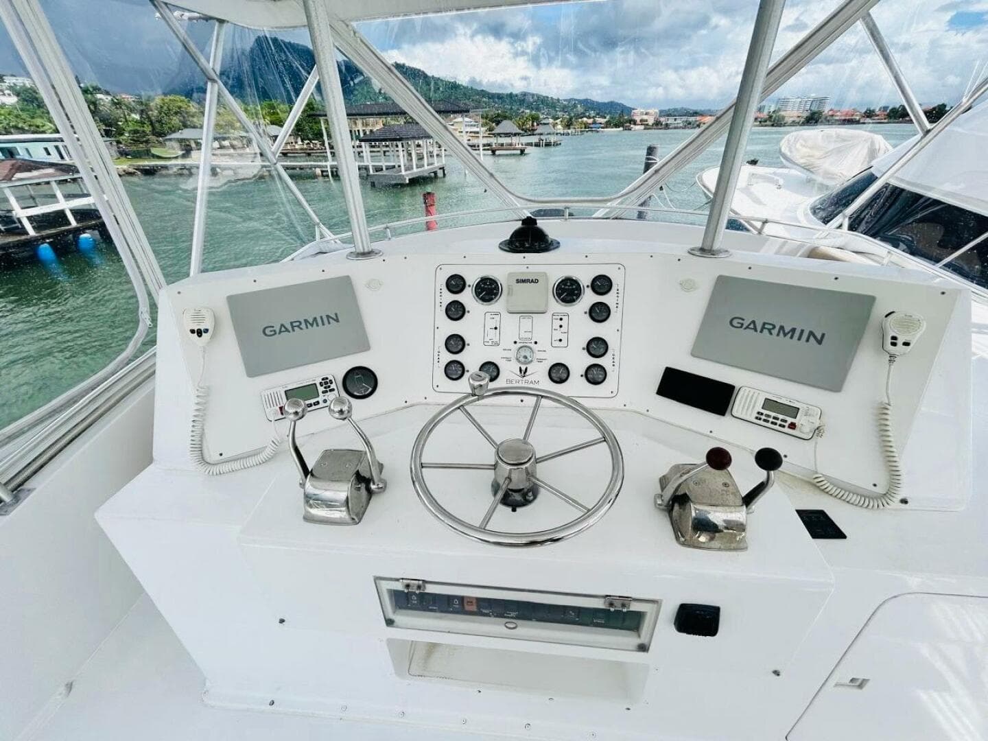 1988 Bertram 54' yacht helm with Garmin navigation, dual controls, and scenic marina view.