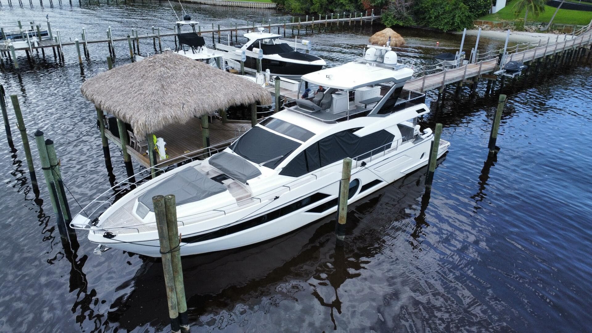 2024 Aicon 66 Vivere yacht docked at a marina with thatched roof hut.