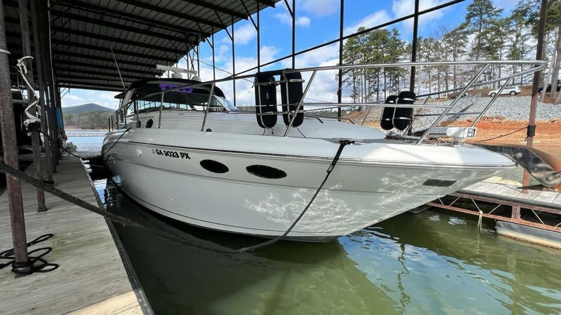 2003 Sea Ray 380 Sundancer docked in a marina, surrounded by calm water and trees.