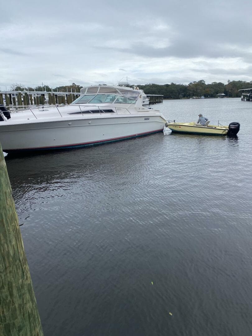 1993 Sea Ray 440 Sundancer docked beside a small yellow boat on a cloudy day.