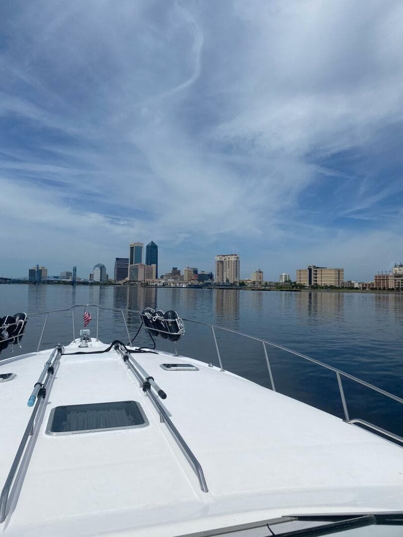 1993 Sea Ray 440 Sundancer cruising towards city skyline under blue sky.