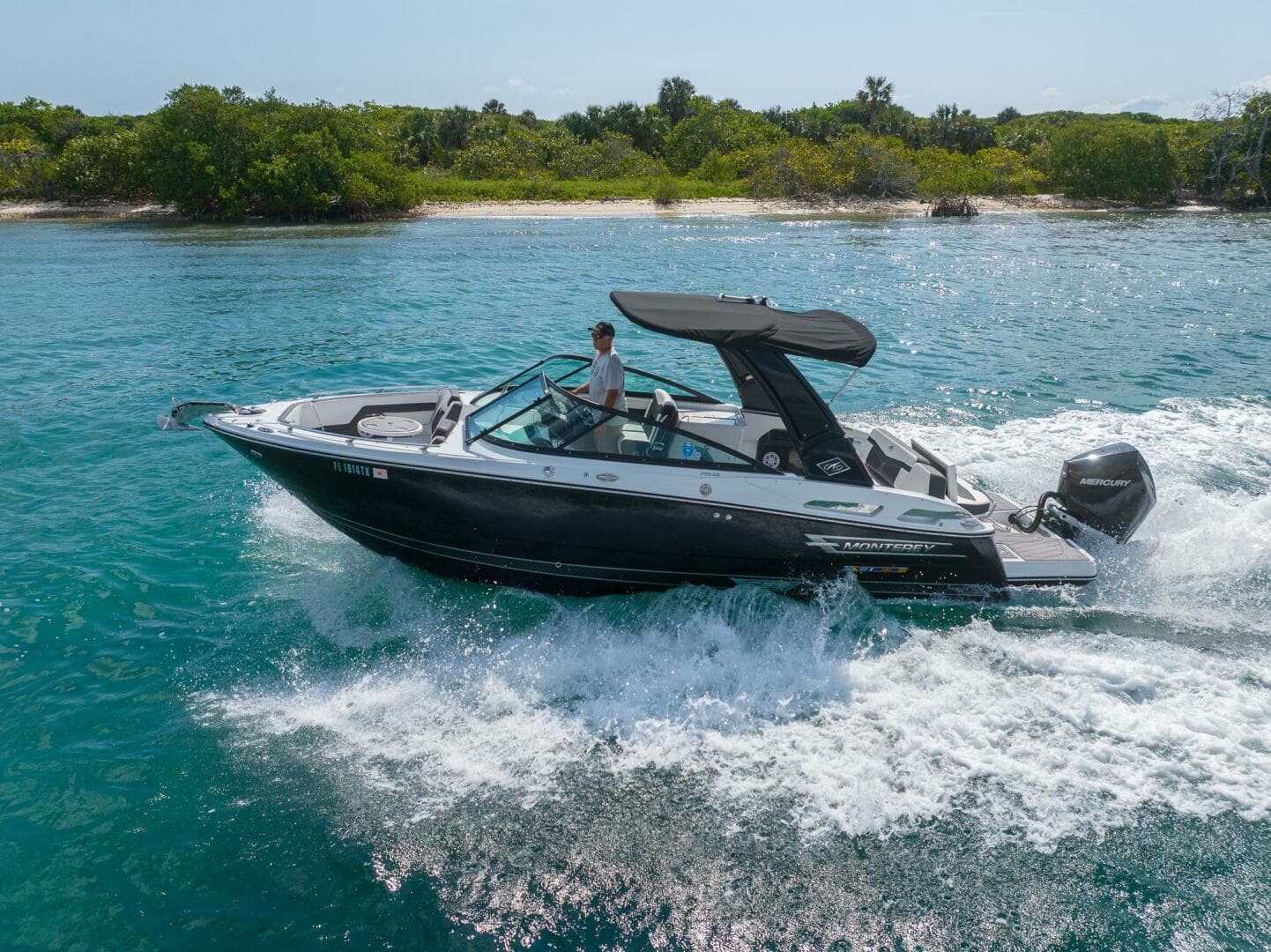 2023 Monterey 255 Super Sport boat cruising on clear blue water near a lush shoreline.