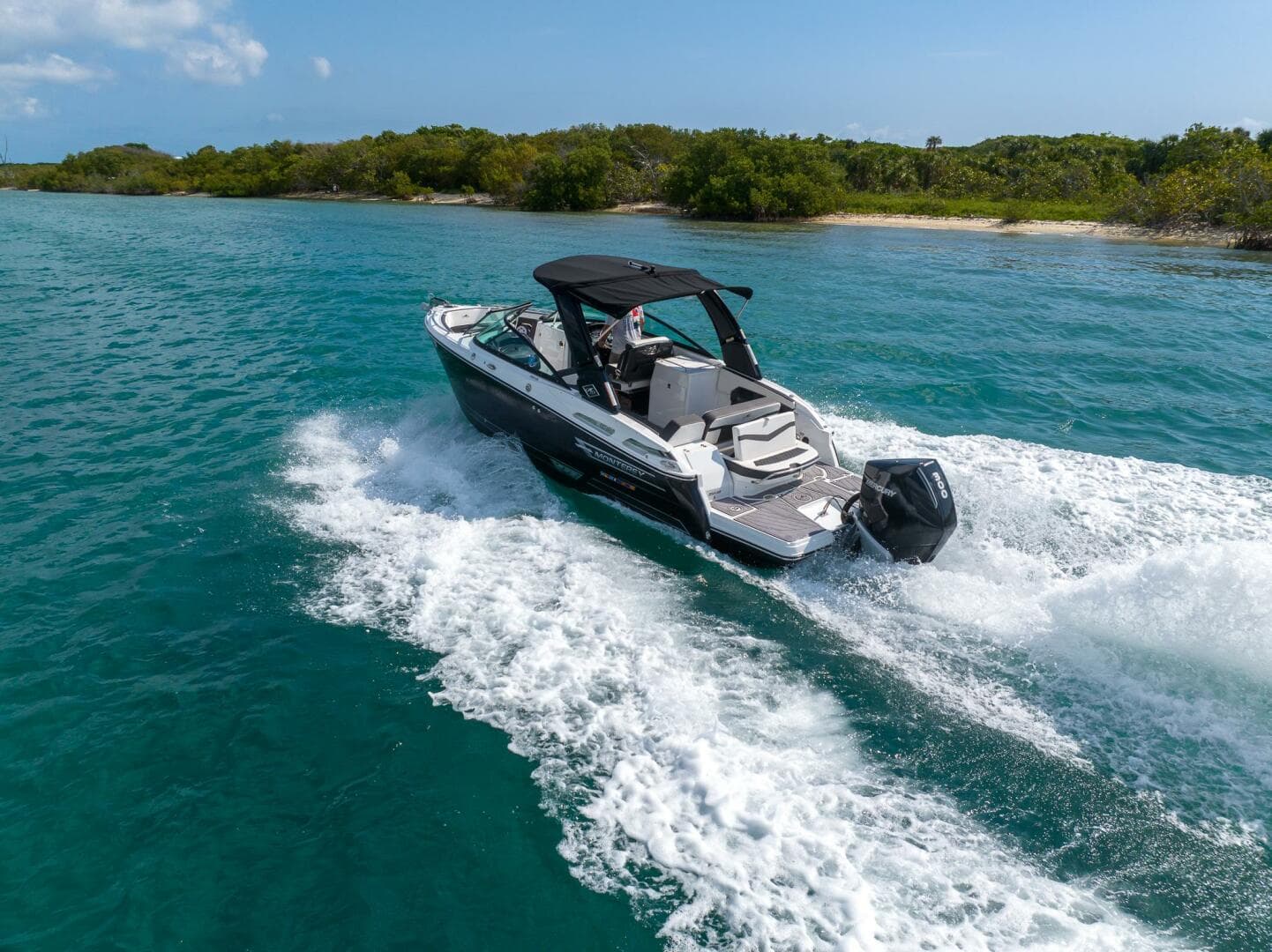 2023 Monterey 255 Super Sport boat cruising on clear blue water near a lush shoreline.
