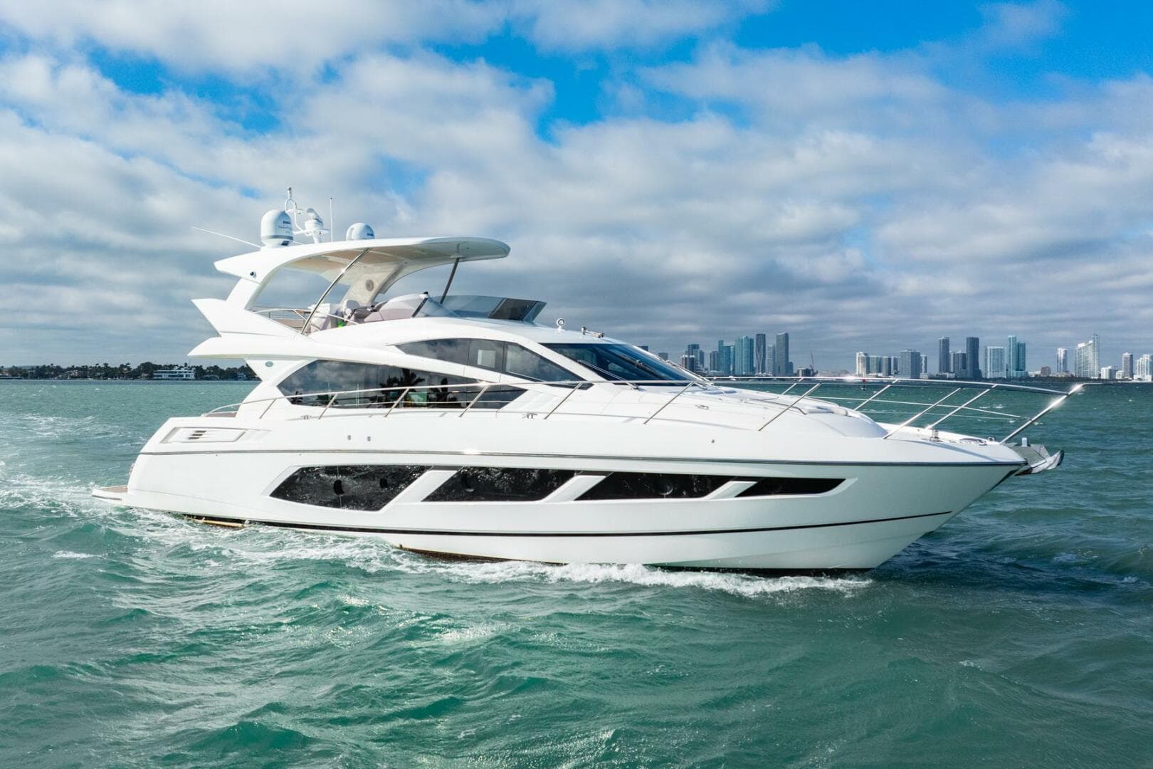2016 Sunseeker Manhattan 65 yacht cruising on open water with city skyline backdrop.