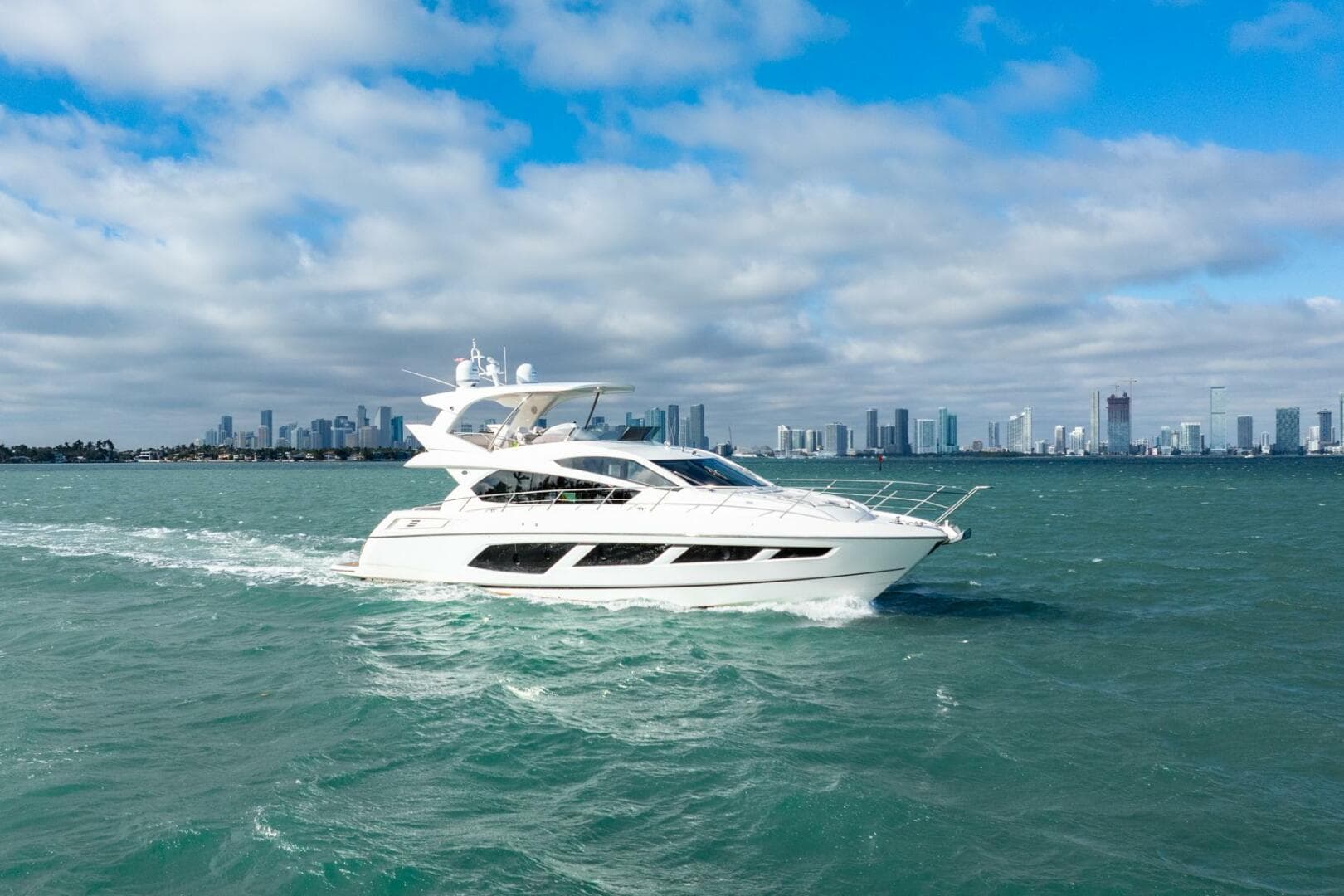 2016 Sunseeker Manhattan 65 yacht cruising on open water with city skyline backdrop.