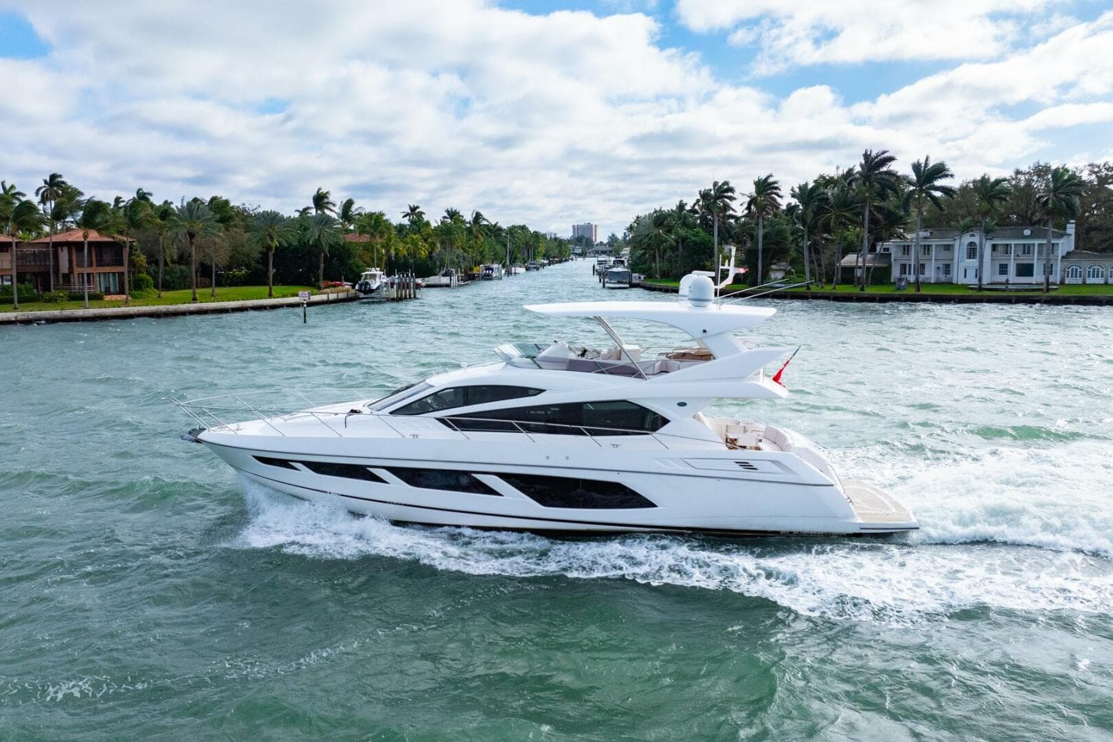 2016 Sunseeker Manhattan 65 yacht cruising on a scenic waterway with palm trees.