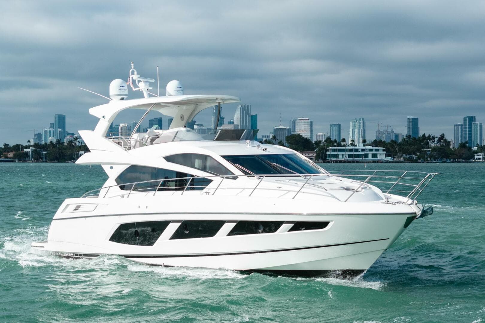 2016 Sunseeker Manhattan 65 yacht cruising on open water with city skyline backdrop.