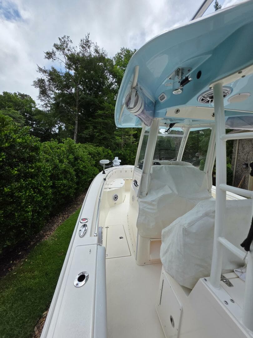 2021 Cobia 301 Center Console boat with covered seating, docked near lush greenery.