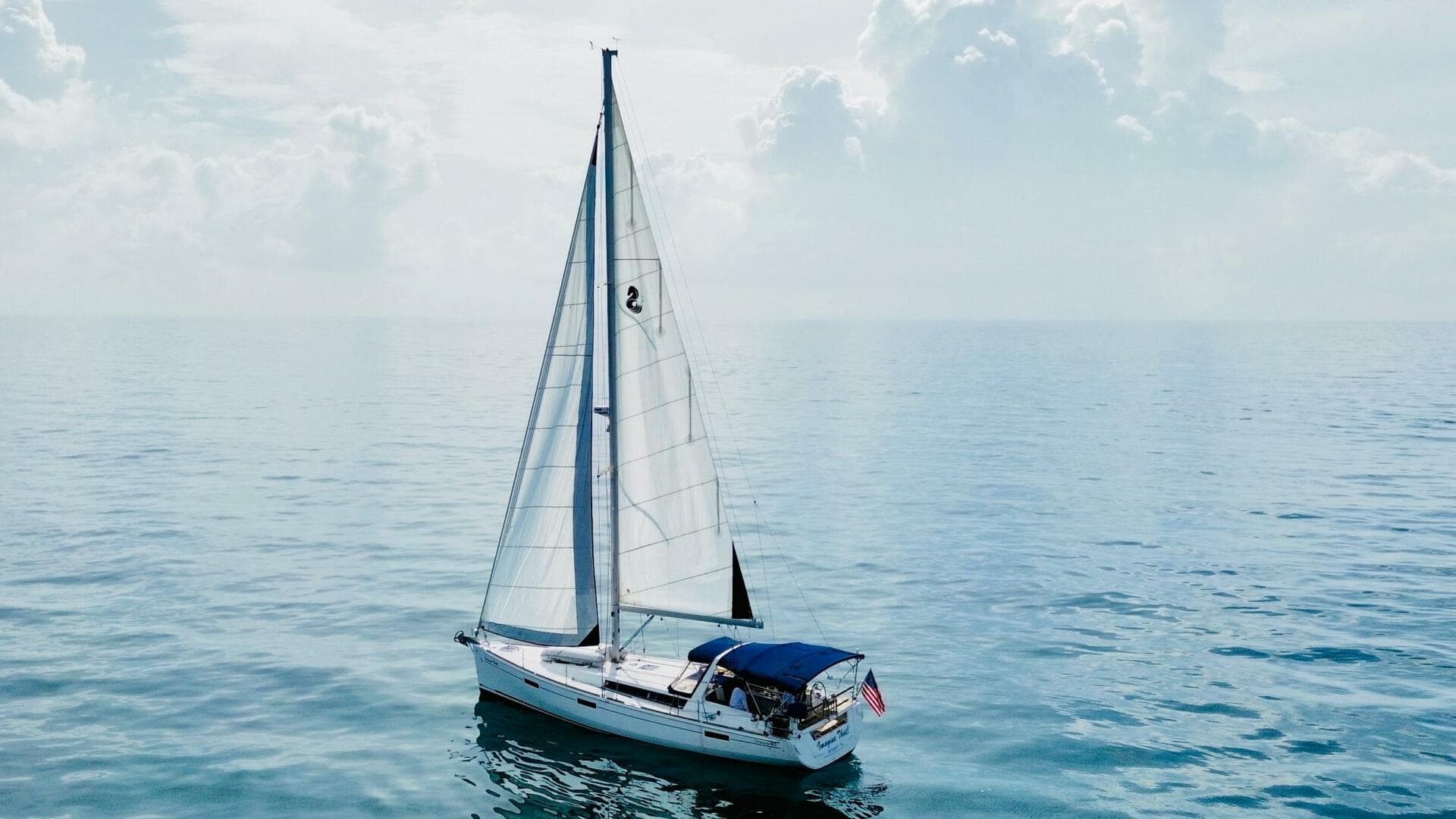 Sailing yacht Beneteau Oceanis 45, 2015 model, on calm ocean waters under cloudy sky.